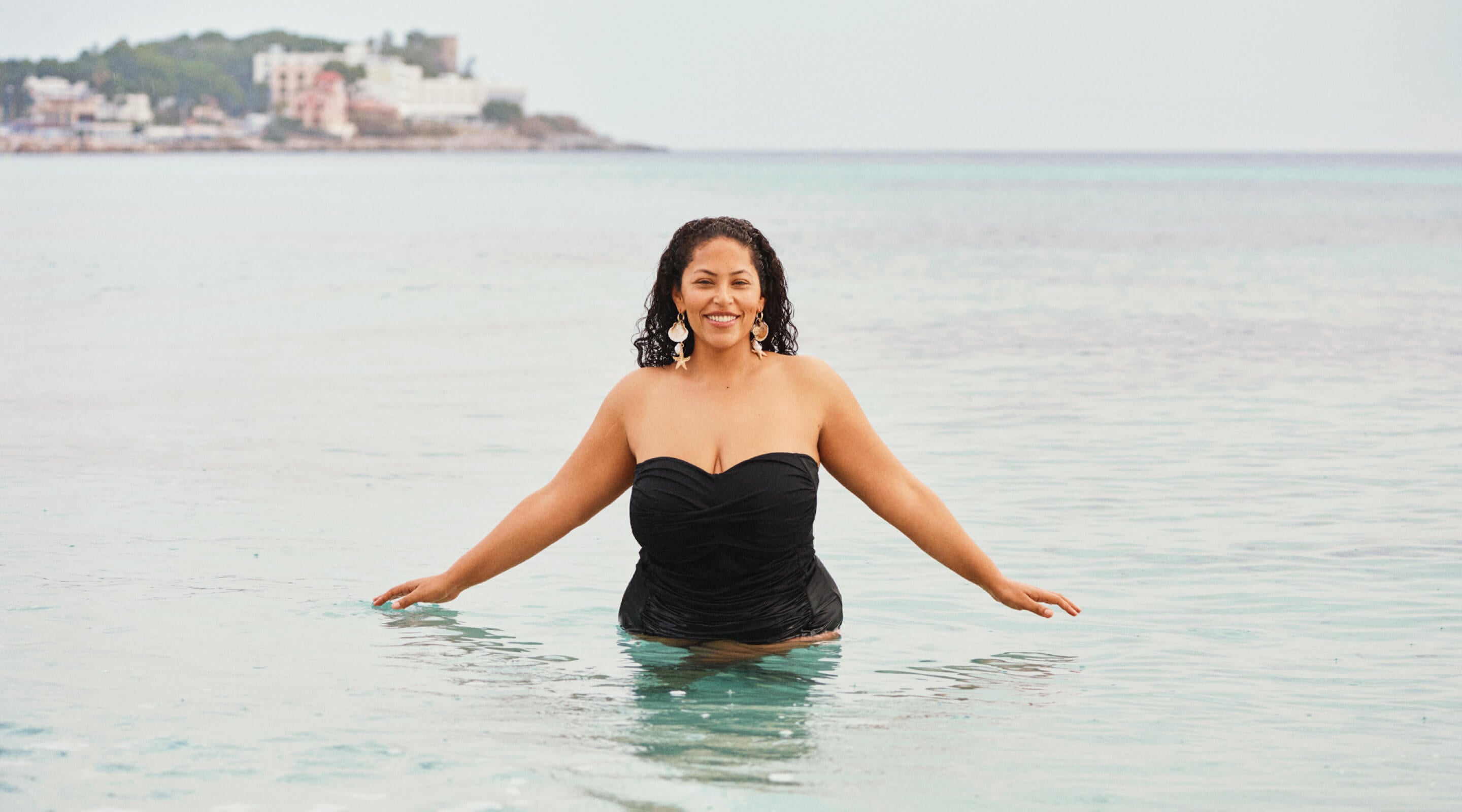 Modell i en hvit bikinioverdel ved havnen med badende rundt.